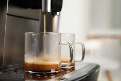 Espresso machine pouring coffee into glass cups against blurred background, closeup. Space for text