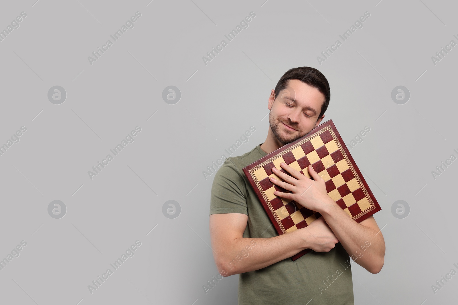 Photo of Handsome man holding chessboard on light grey background. Space for text