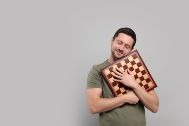 Photo of Handsome man holding chessboard on light grey background. Space for text