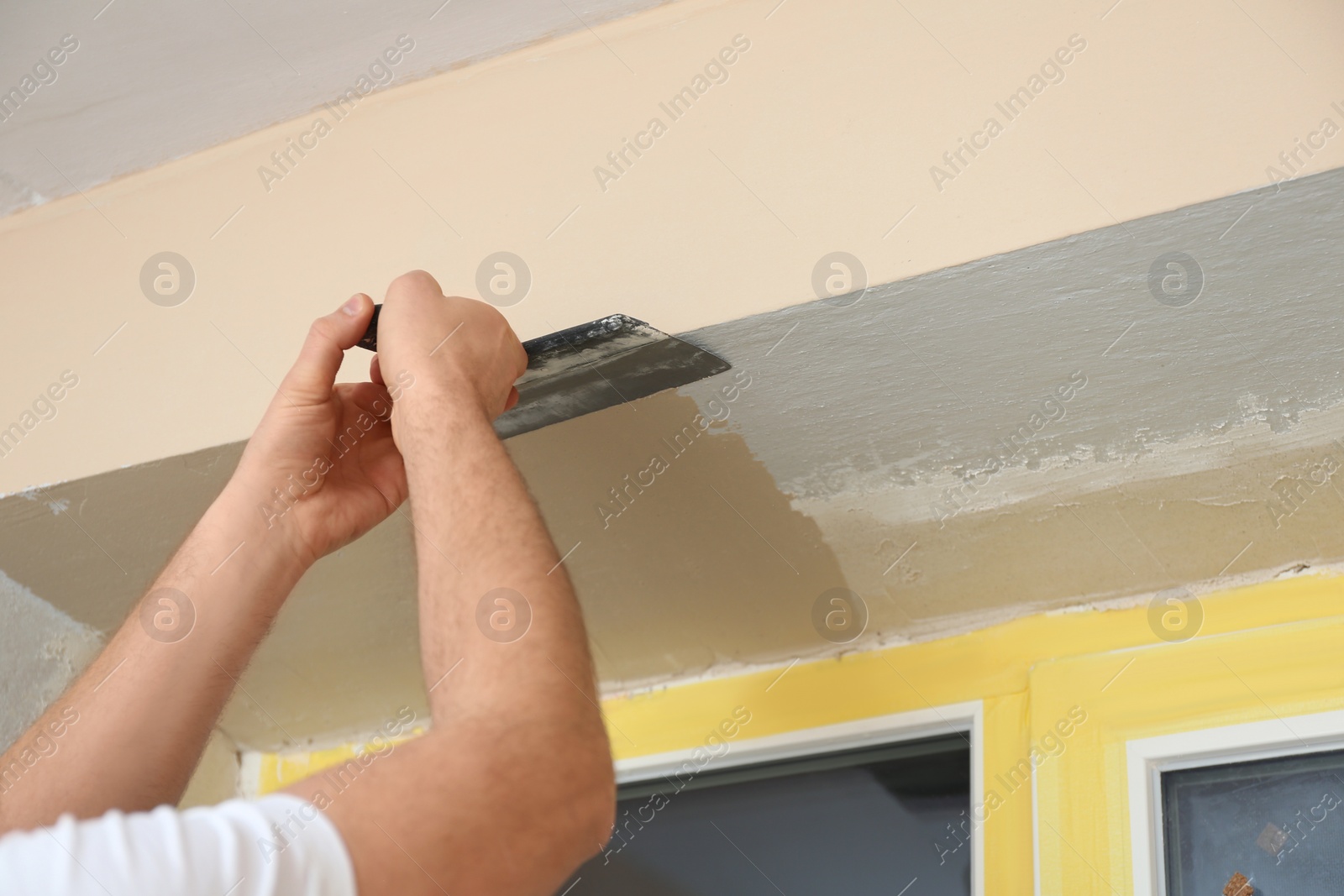 Photo of Man plastering window area with putty knife indoors, closeup. Interior repair