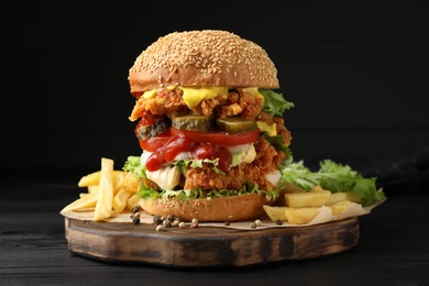 Photo of Delicious burger with crispy chicken patty and french fries on black wooden table