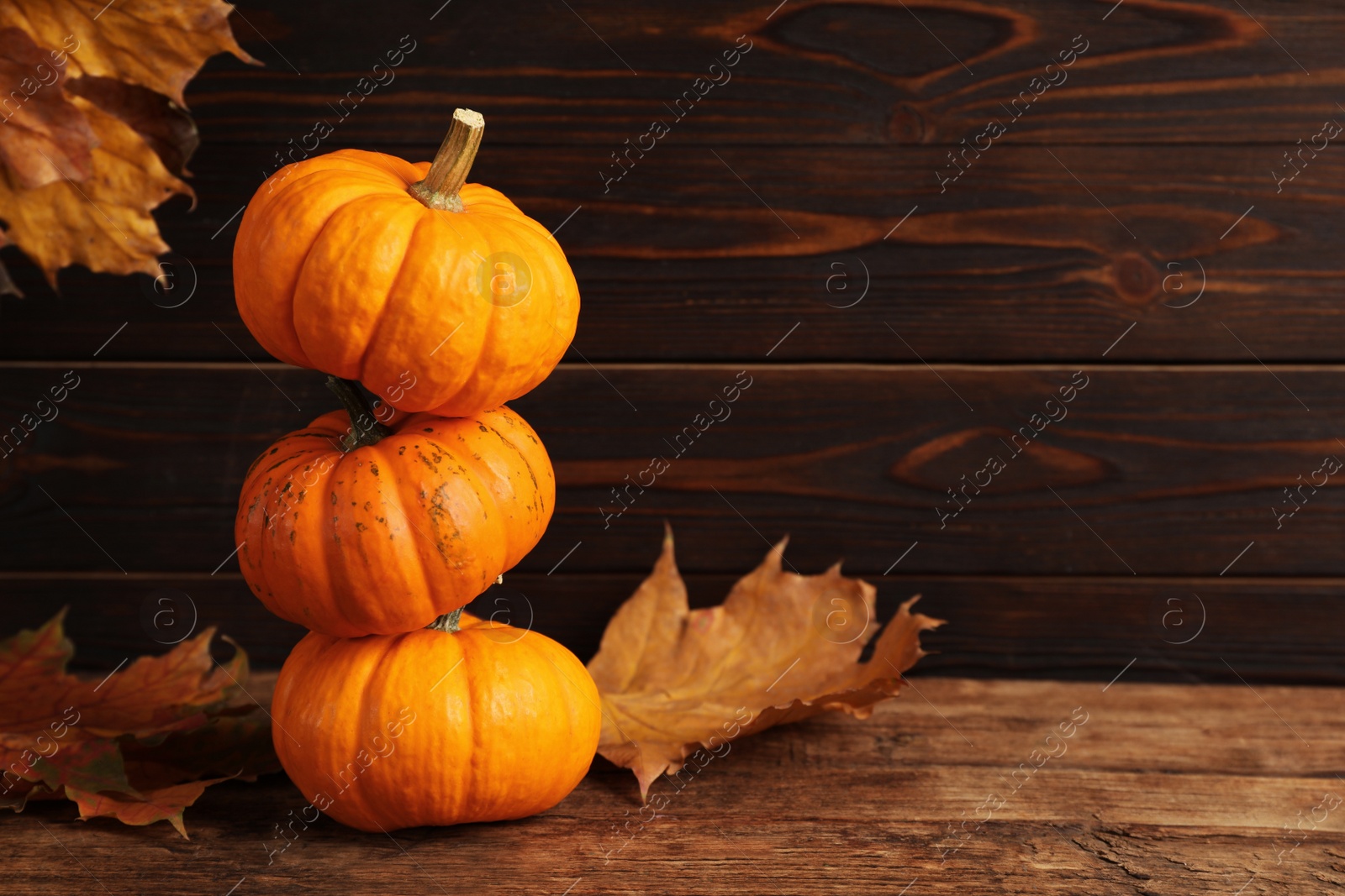 Photo of Stack of fresh ripe pumpkins and dry leaves on wooden table, space for text