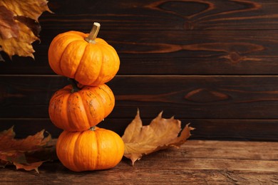 Stack of fresh ripe pumpkins and dry leaves on wooden table, space for text