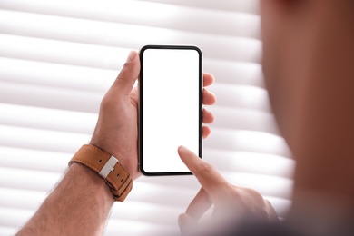 Photo of Man using mobile phone with empty screen near window indoors, closeup