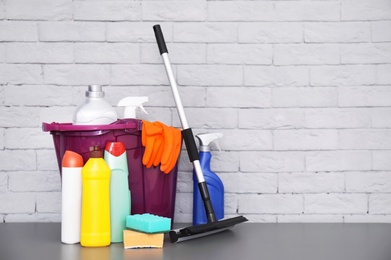 Set of cleaning supplies on table near brick wall