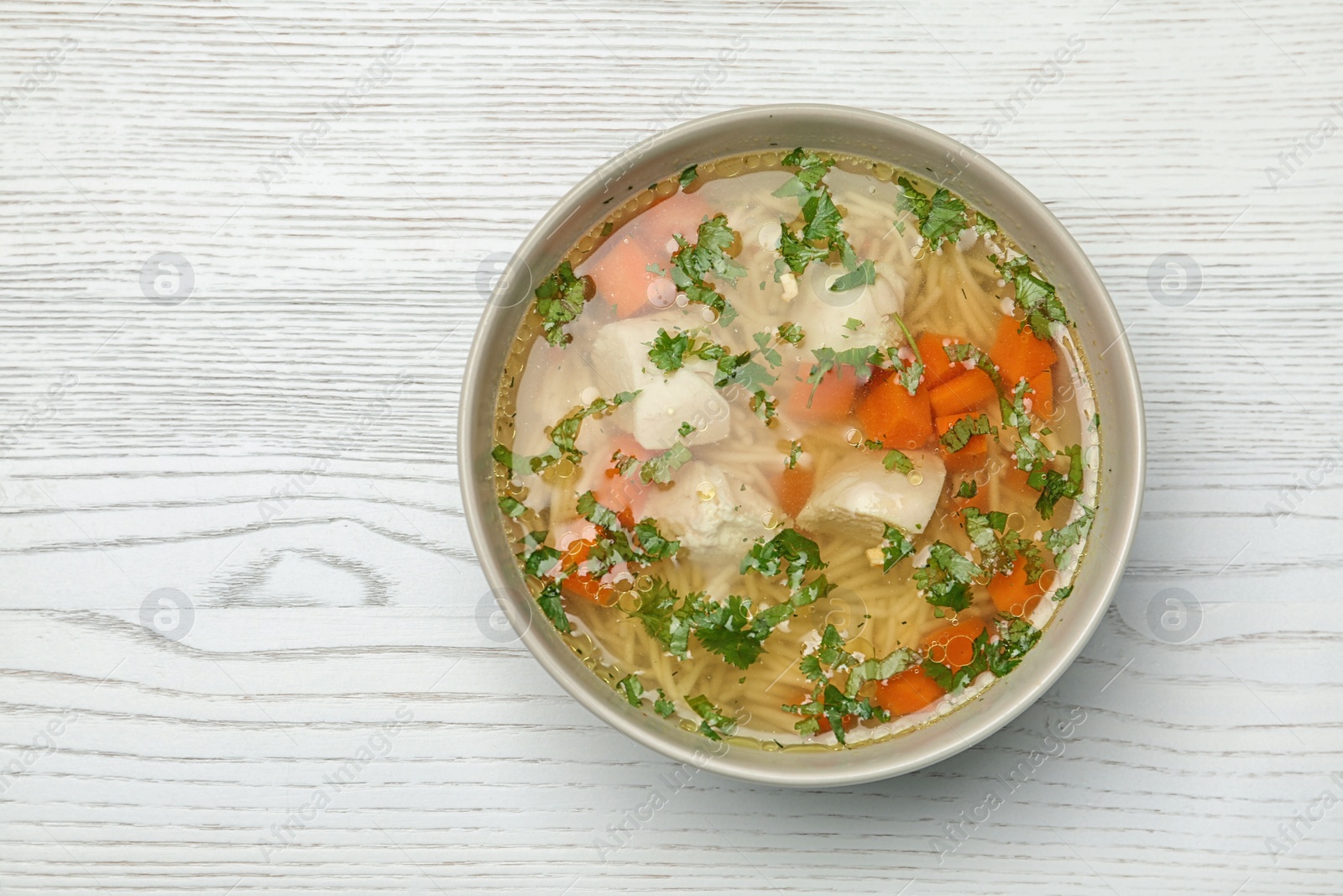 Photo of Bowl of fresh homemade chicken soup on wooden background, top view with space for text