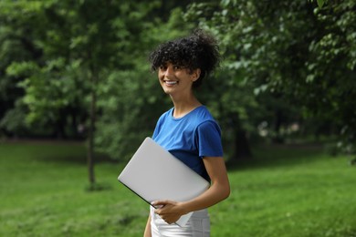 Photo of Happy young woman holding modern laptop in park