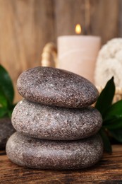 Photo of Stacked spa stones, bamboo leaves and candle on wooden table, closeup