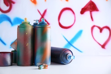 Many spray paint cans near white wall with different drawn symbols, space for text