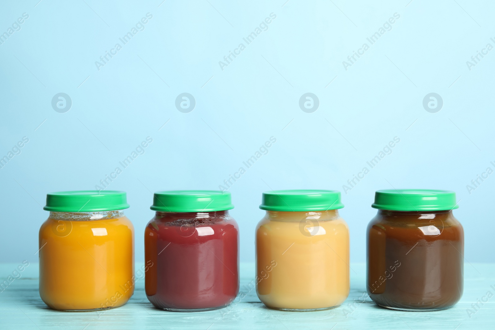 Photo of Jars with baby food on wooden table against light blue background, space for text