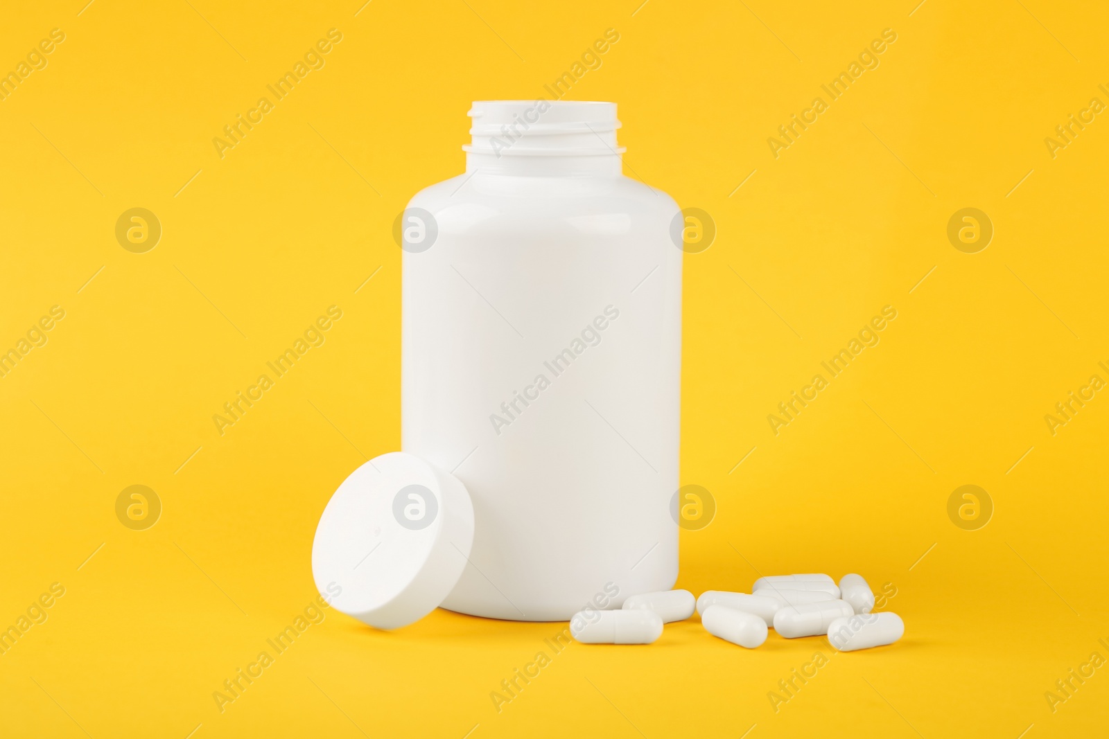 Photo of Blank white jar with vitamin capsules on yellow background, space for text