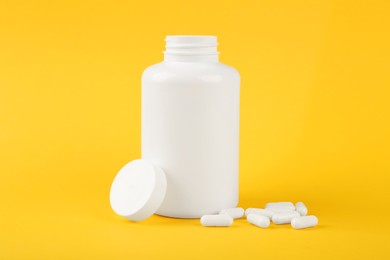 Photo of Blank white jar with vitamin capsules on yellow background, space for text