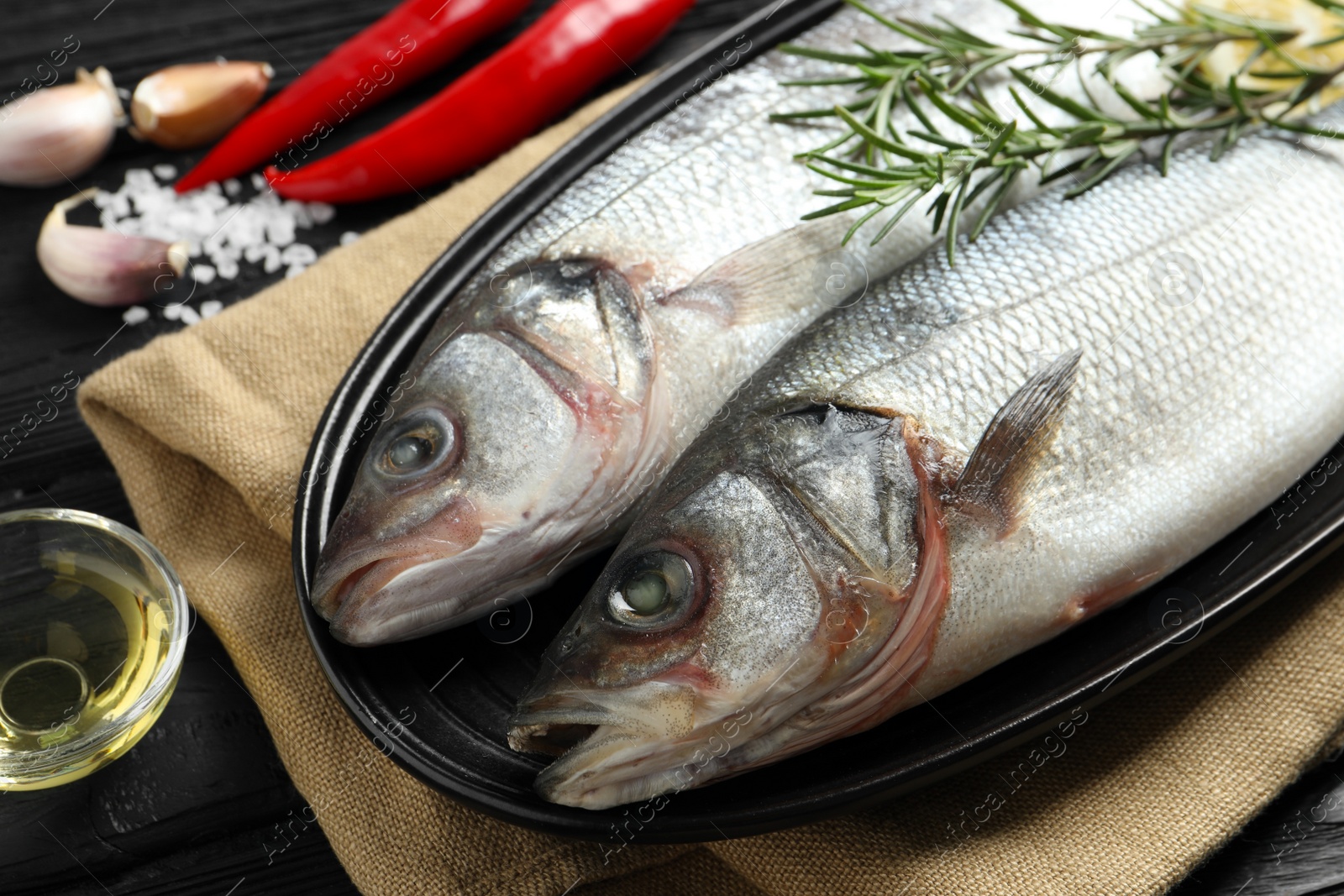 Photo of Tasty sea bass fish with spices on black wooden table, closeup