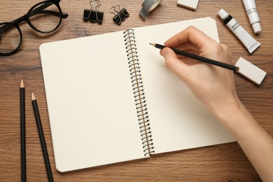 Photo of Woman with pencil and blank sketchbook at wooden table, top view