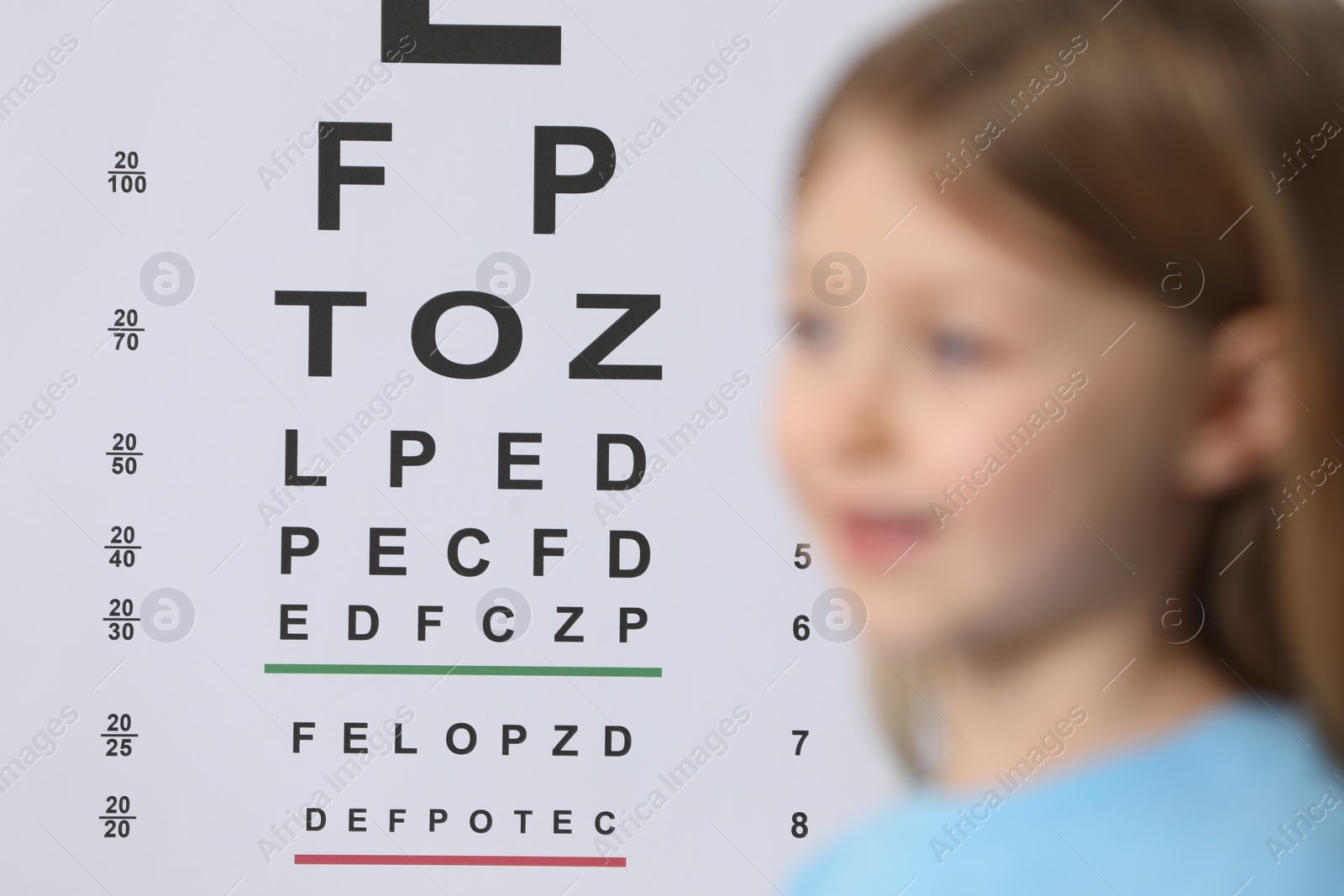 Photo of Cute little girl against vision test chart, selective focus