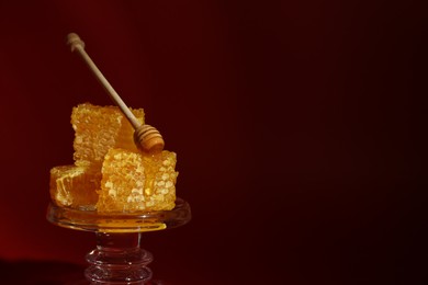Photo of Natural honeycombs and wooden dipper on stand against burgundy background, space for text