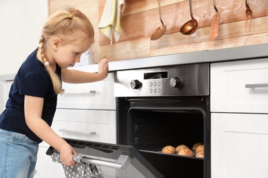 Little girl checking cookies in oven at home