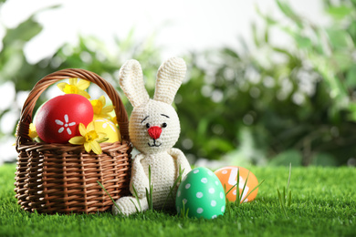 Colorful Easter eggs, toy rabbit and daffodil flowers in green grass. Space for text