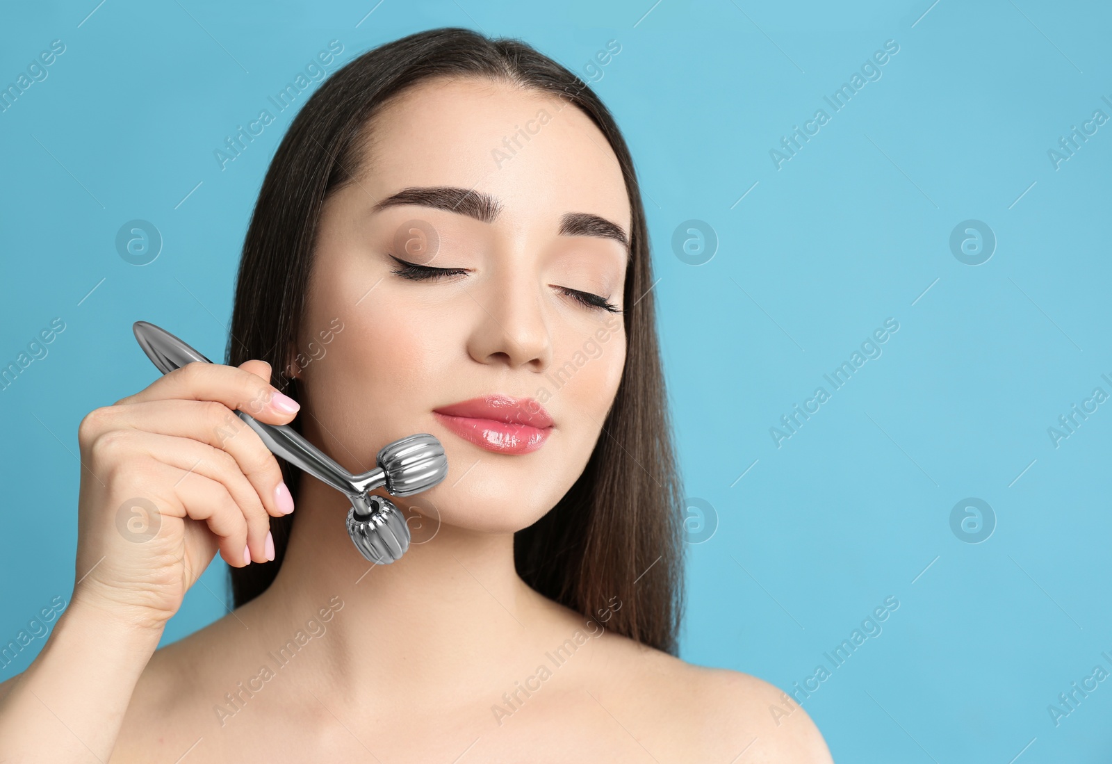 Photo of Woman using metal face roller on light grey  background, space for text