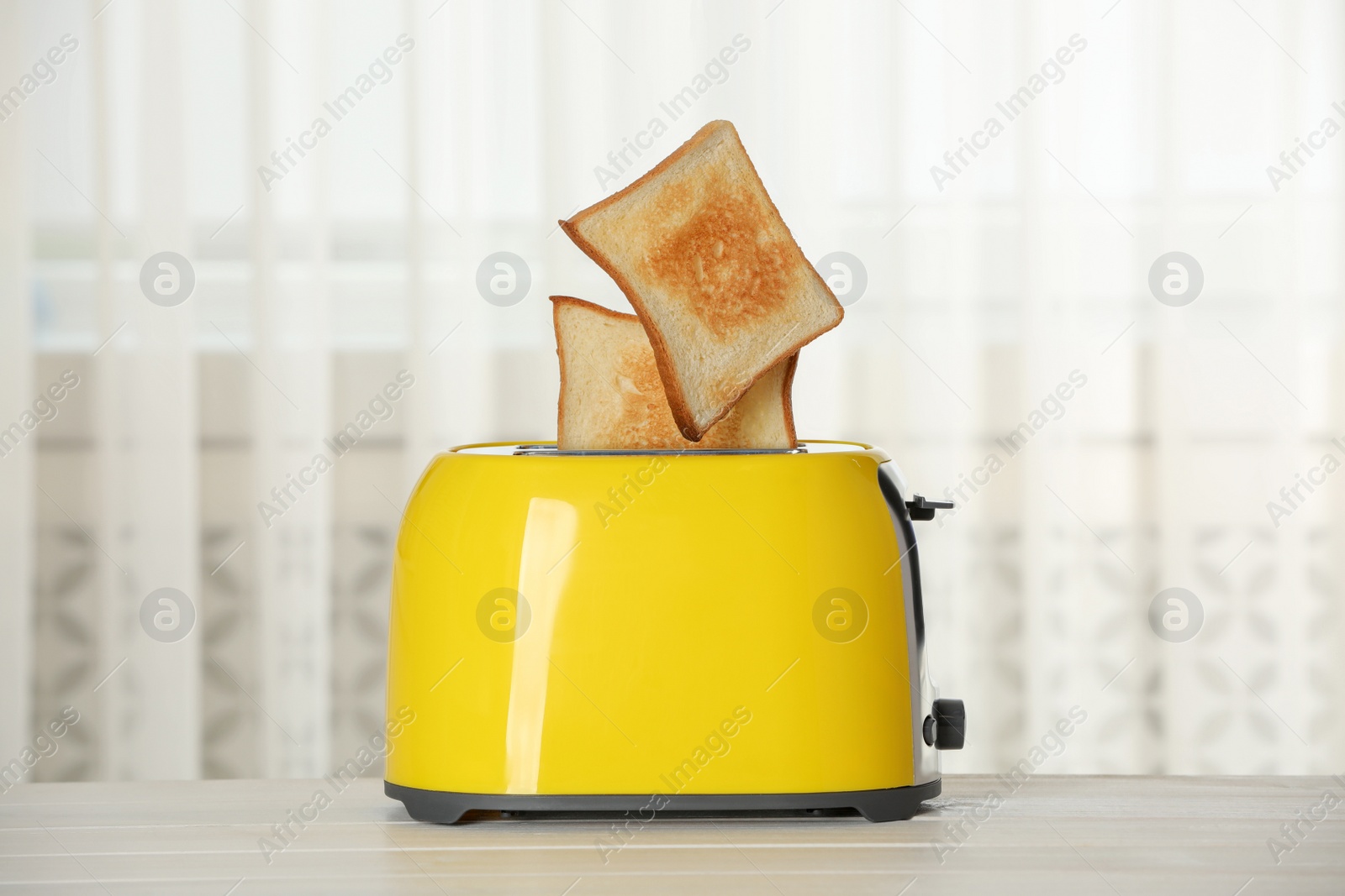 Photo of Bread slices popping up out of electric toaster on wooden table