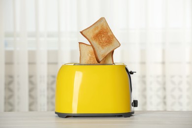 Photo of Bread slices popping up out of electric toaster on wooden table