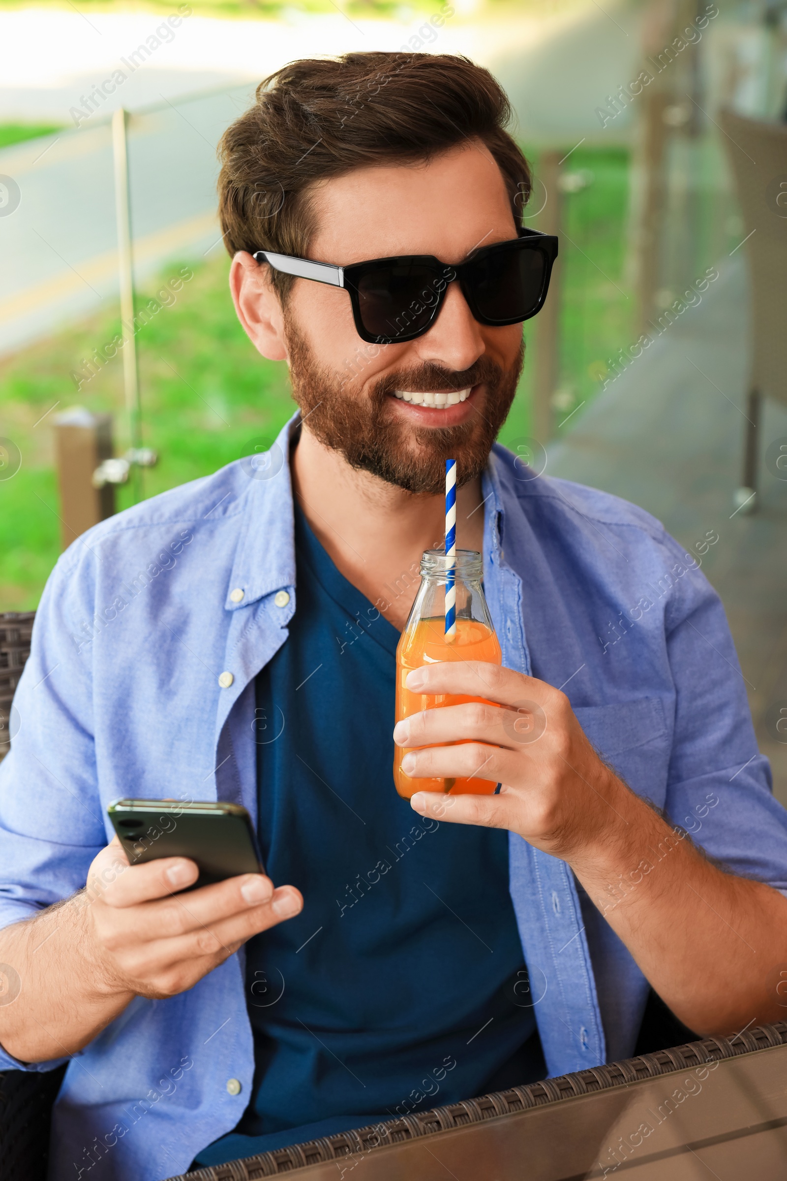 Photo of Handsome man with bottle of delicious juice in outdoor cafe