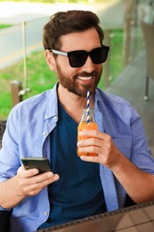Photo of Handsome man with bottle of delicious juice in outdoor cafe