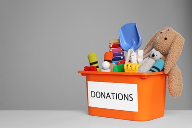 Photo of Donation box with different toys on white table against grey background. Space for text