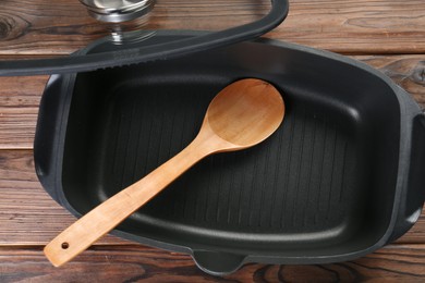 Black pot and spoon on wooden table, flat lay