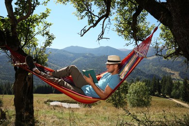Photo of Handsome man reading book in hammock outdoors on sunny day