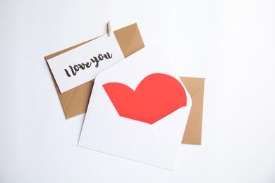 Card with phrase I Love You, envelopes and red heart on white background, flat lay