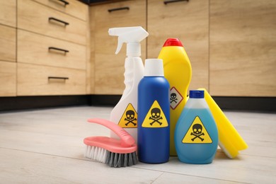Photo of Bottles of toxic household chemicals with warning signs, scouring sponge and brush on floor indoors