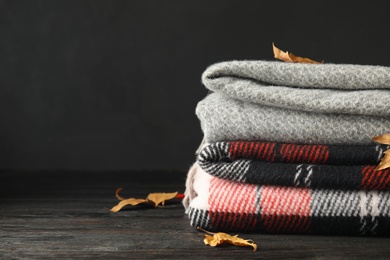 Stack of soft plaids and dry leaves on black wooden table, closeup. Space for text