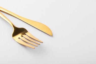 Photo of Stylish cutlery. Golden knife and fork on gray background, closeup. Space for text