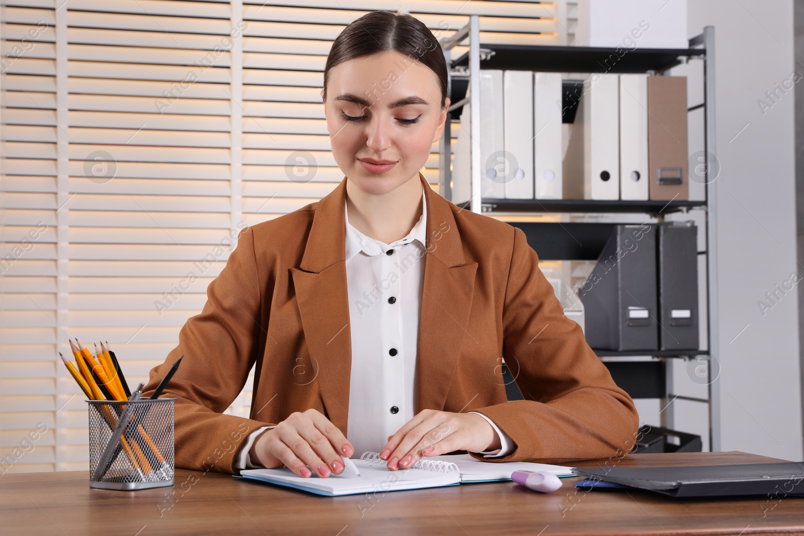 Photo of Woman taking notes at wooden table in office