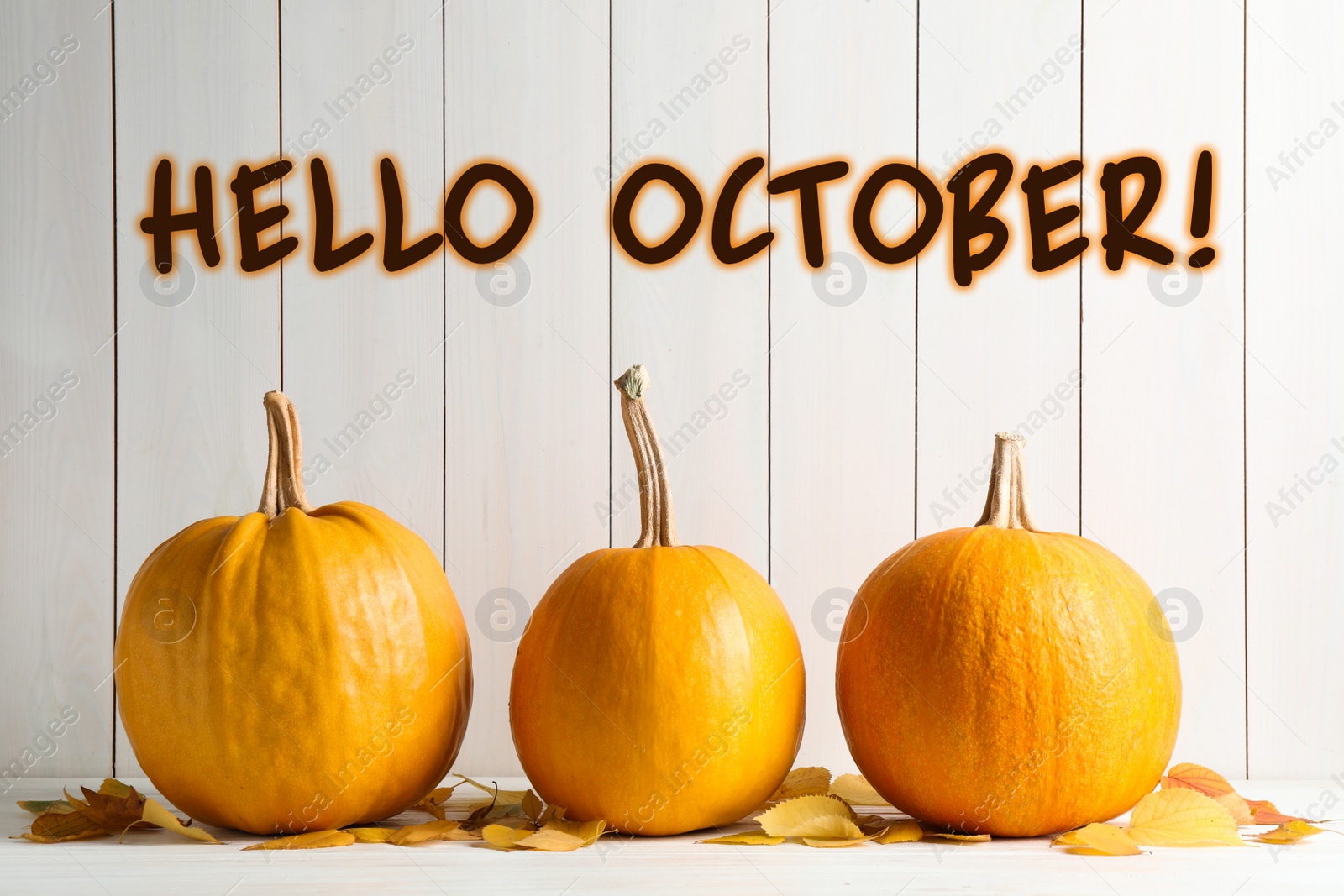 Image of Hello October card. Pumpkins and autumn leaves on white table 