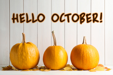 Image of Hello October card. Pumpkins and autumn leaves on white table 