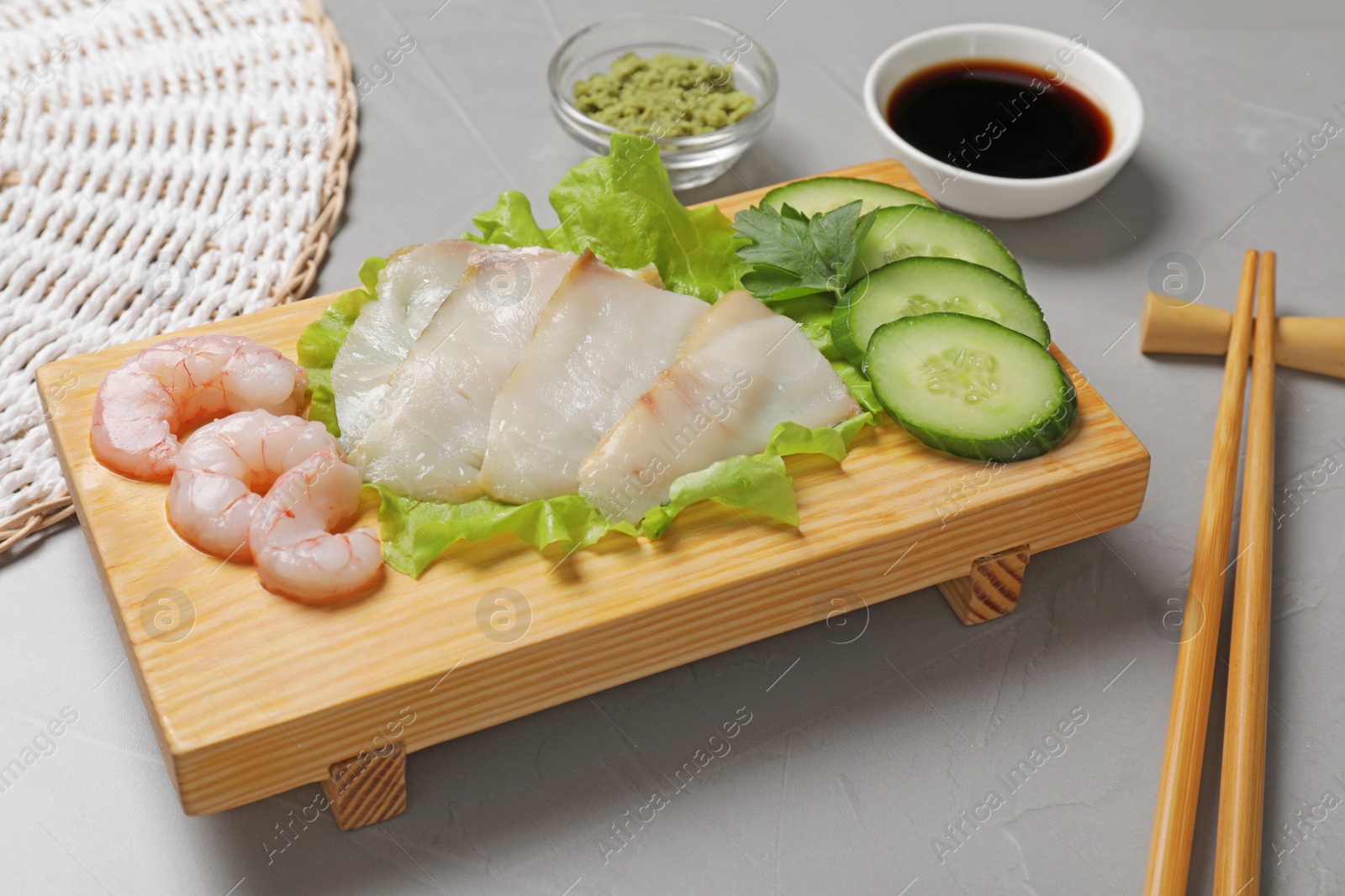 Photo of Sashimi set served with cucumber, lettuce, soy sauce and vasabi on light grey table