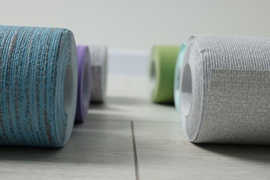 Different wallpaper rolls on light wooden floor, closeup