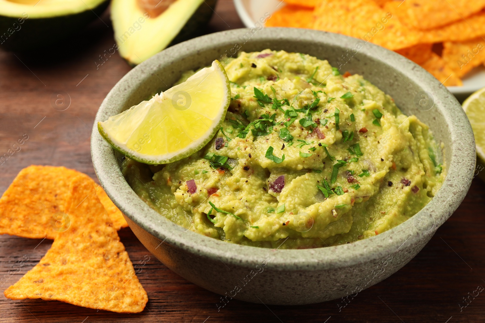 Photo of Bowl of delicious guacamole, lime and nachos chips on wooden table, closeup