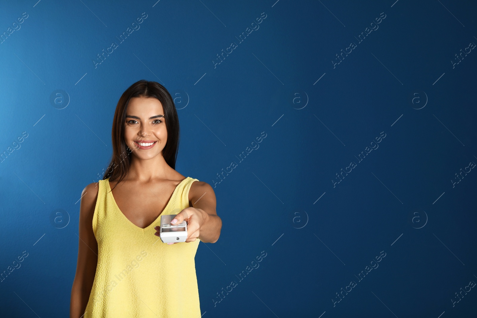 Photo of Young woman with air conditioner remote on blue background. Space for text