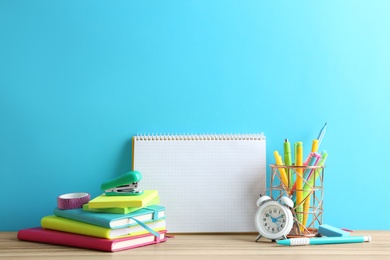 Photo of Different school stationery and blank notebook on table near light blue wall. Space for text