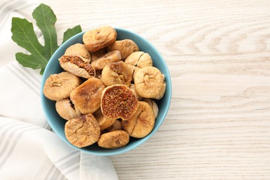 Photo of Bowl with tasty dried figs and green leaf on white wooden table, flat lay. Space for text