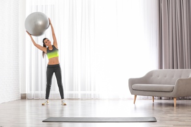 Young woman doing exercise with fitness ball at home. Space for text