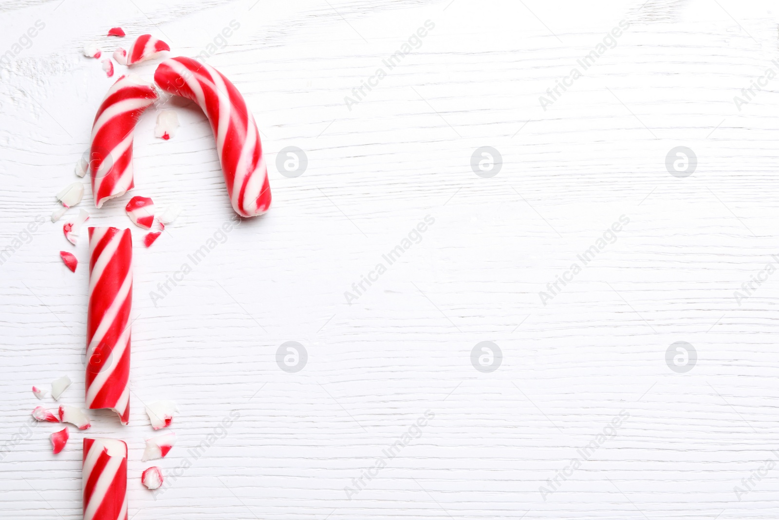 Photo of Broken sweet Christmas candy cane on white wooden table, top view. Space for text