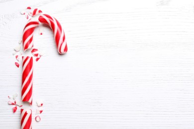 Broken sweet Christmas candy cane on white wooden table, top view. Space for text