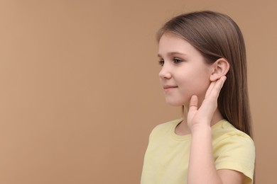 Little girl with hearing problem on pale brown background, space for text