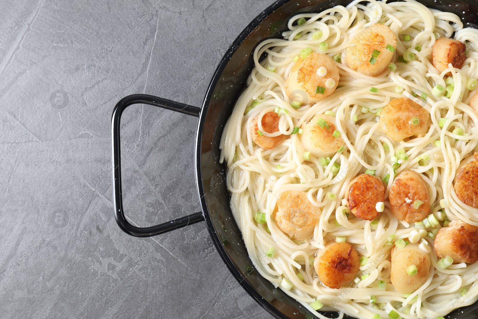 Photo of Delicious scallop pasta with green onion on grey table, top view