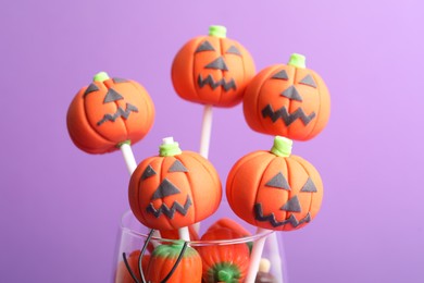 Photo of Delicious pumpkin shaped cake pops on violet background, closeup. Halloween treat