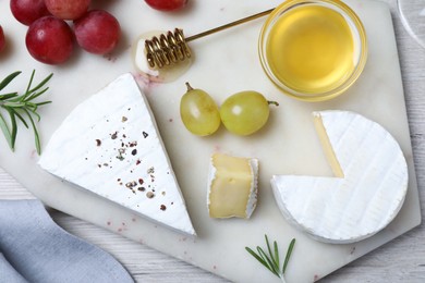 Photo of Tasty brie cheese with honey, rosemary and grapes on white board, flat lay